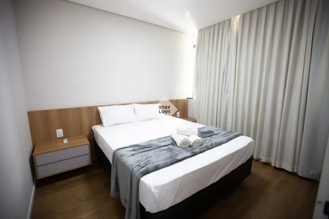 Cantinho de leitura em sala de apartamento com poltrona, abajur e prateleira de livros