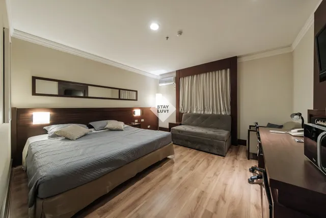 Studio de apartamento dividido em zonas com estante aberta, sofá claro e cama ao fundo