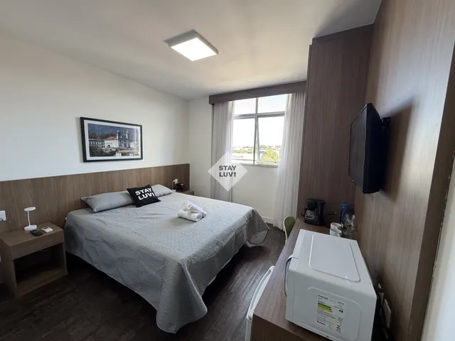 Studio decorado para temporada com cama de casal, cozinha compacta e mesa de trabalho junto à janela